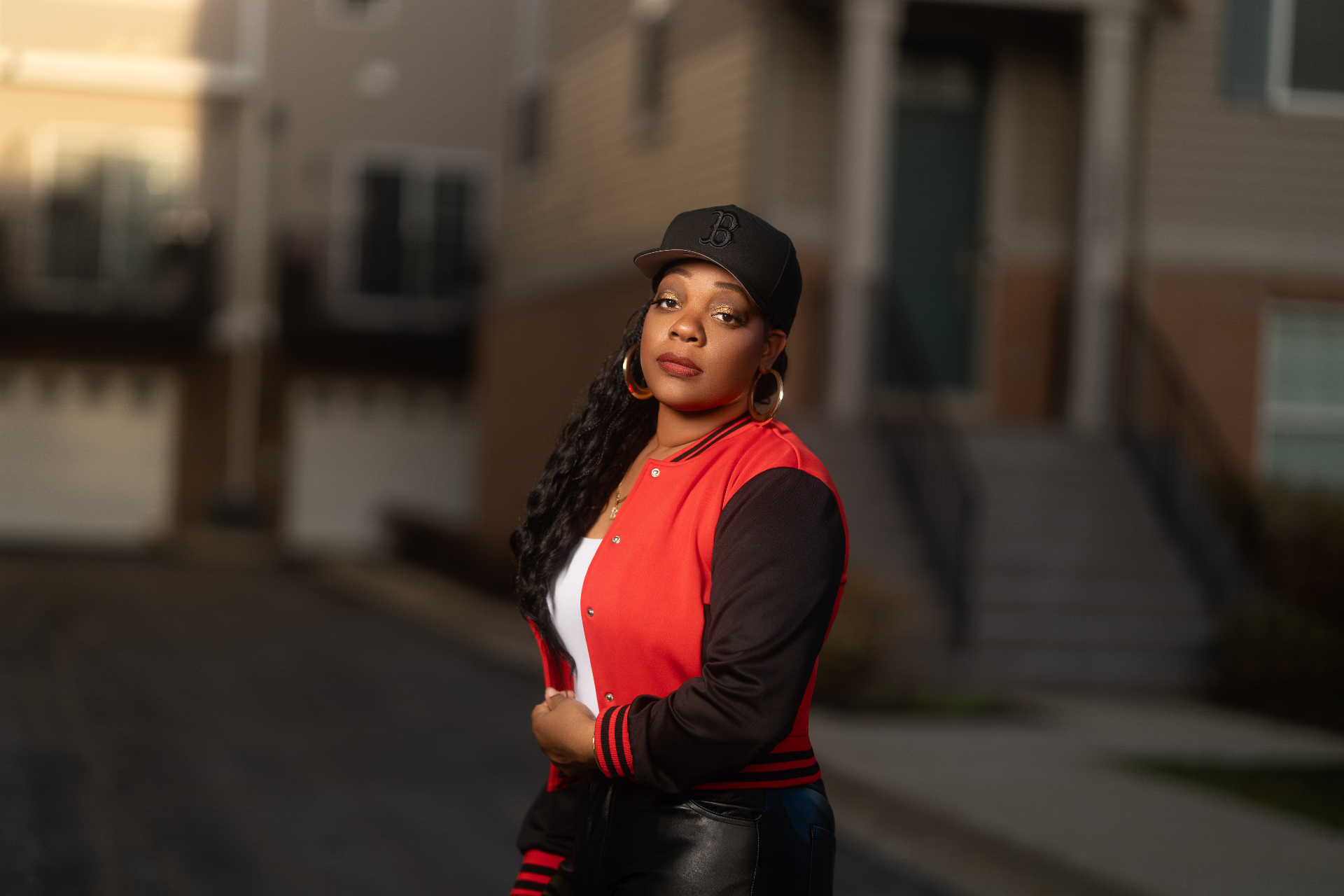 Editorial portrait in red varsity jacket and B cap at dusk
